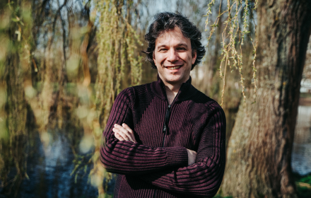 Foto van een man die met gekruisde armen staat, achter hem zijn bomen